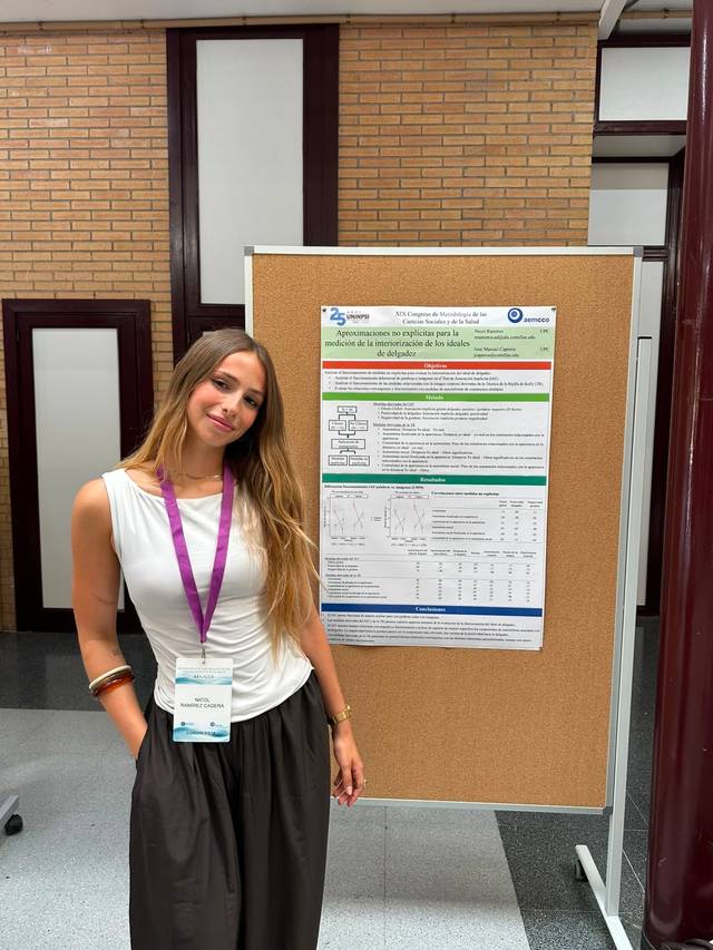 Una mujer posa junto a un póster en un evento académico.