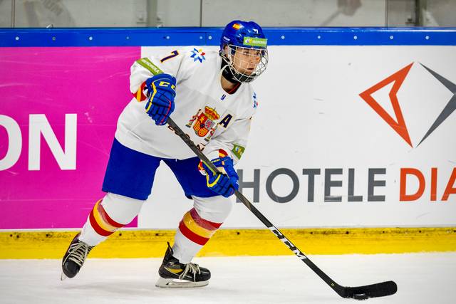 Jugador de hockey sobre hielo en pleno partido, vistiendo uniforme blanco con detalles azules y rojos.