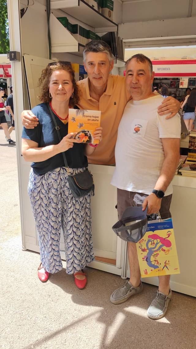 Tres personas posan sonrientes frente a un puesto de libros en un evento.