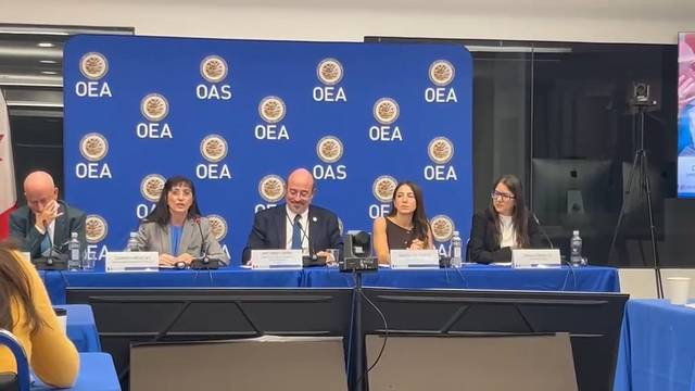La imagen muestra a un grupo de personas sentadas en una mesa durante una conferencia de prensa en la OEA.