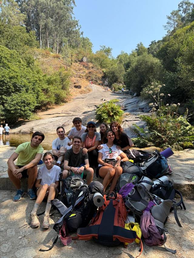 Un grupo de personas sonrientes posando en un entorno natural con mochilas y vegetación alrededor.