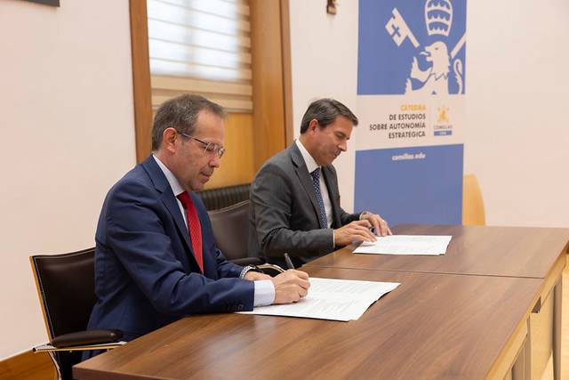 Dos hombres están firmando documentos en una mesa durante un evento oficial.