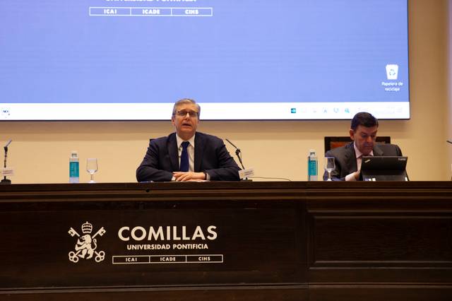 Dos hombres participan en un evento en un auditorio de la Universidad Pontificia Comillas.