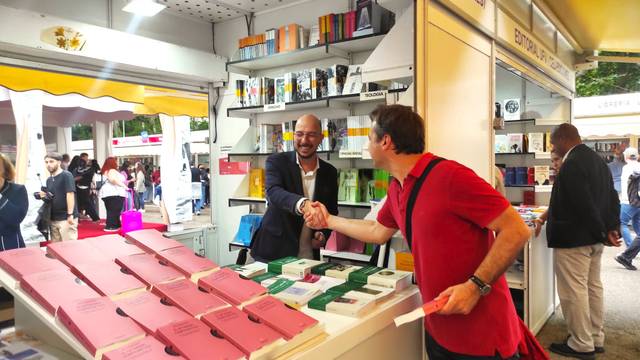 Two men shaking hands at a book stall in a busy outdoor market.