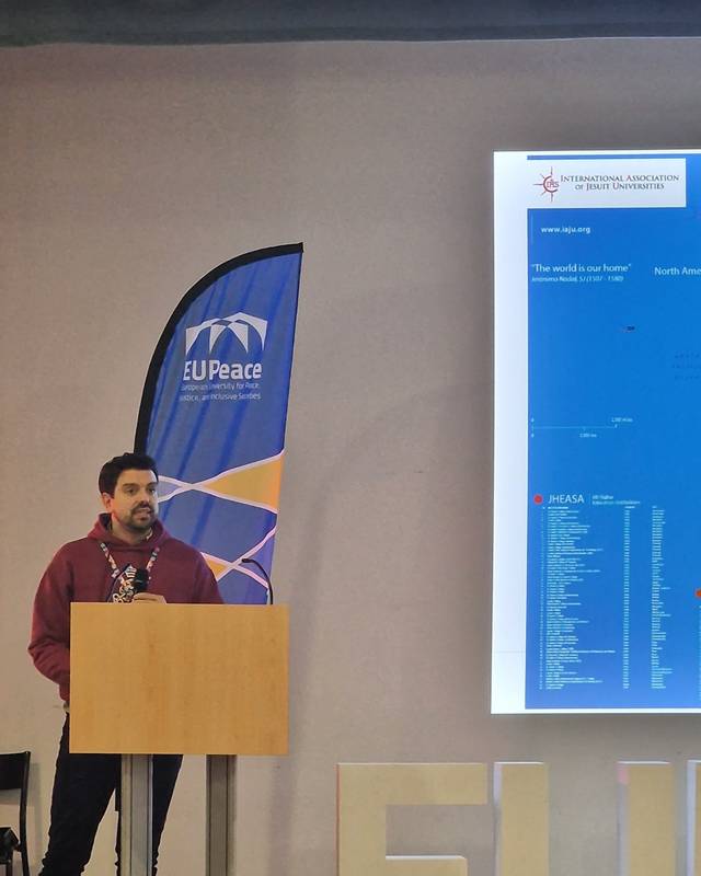 Una persona presenta en una conferencia mientras se proyecta una diapositiva en la pantalla.