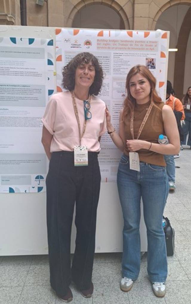 Dos mujeres posan juntas frente a un cartel en un evento académico.