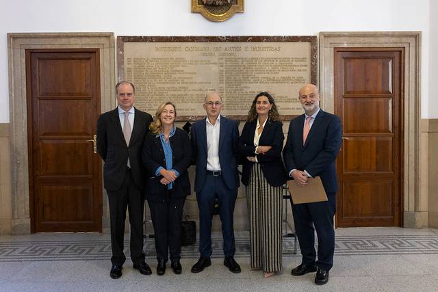 Un grupo de cinco personas posan frente a una pared con inscripciones en un entorno interior apegado a la formalidad.