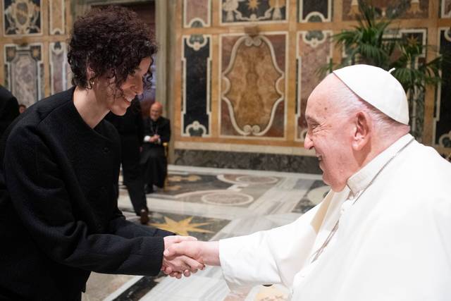 El Papa Francisco estrecha la mano de una mujer en un interior adornado con mosaicos.