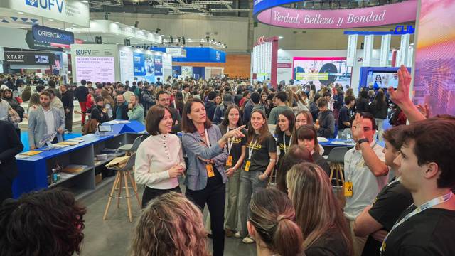 Un grupo de personas interactuando en un evento concurrido, con presentaciones y actividades a su alrededor.