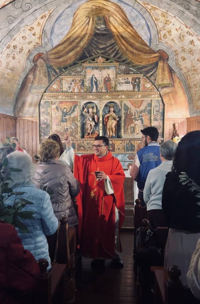 Un sacerdote vestido con ropas litúrgicas rojas celebra una misa ante una congregación en una capilla decorada con arte religioso.