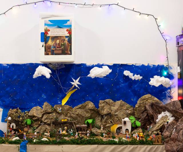 La imagen muestra un belén decorado con figuras y elementos naturales, bajo un fondo de un cielo estrellado con nubes y una estrella brillante.