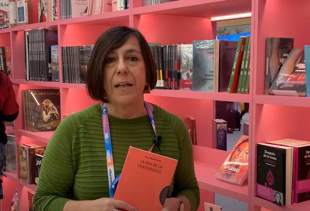 Belén Recio Godoy sostiene un libro en una librería con estanterías rosas llenas de libros.