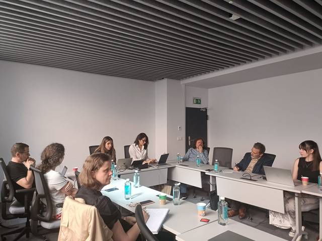 Un grupo de personas se encuentra en una sala de reuniones, conversando y trabajando en un ambiente profesional.