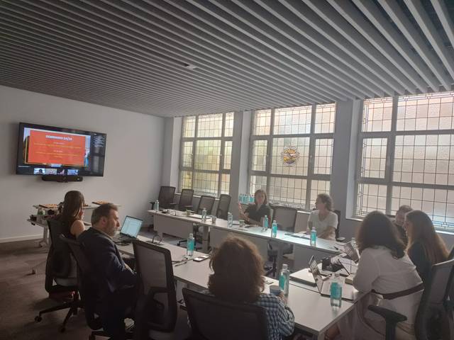 Una reunión en una sala con varios asistentes discutiendo frente a una pantalla.