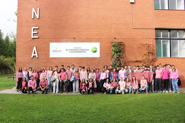 Grupo de estudiantes vestidos de rosa frente a un edificio de la escuela de ingeniería agrícola.