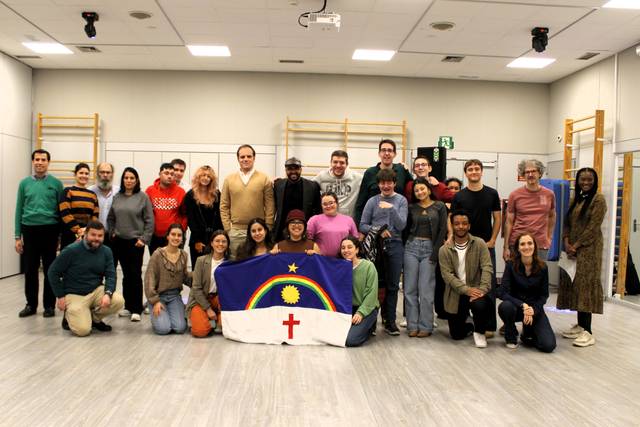 Un grupo diverso de personas posando juntas en un espacio interior con una bandera en el centro.
