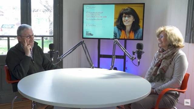 Two people sitting at a table with microphones in a podcast studio, with a presentation screen showing a tribute to Hilary Mantel.