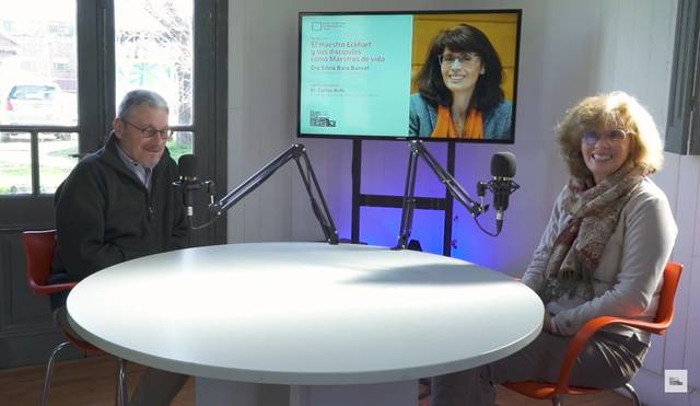 Two people sitting at a table in a studio, smiling as they prepare for a radio or podcast interview.