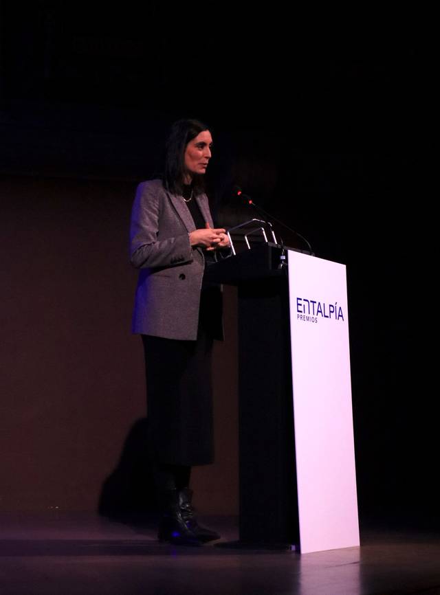 Una mujer está dando una presentación en un evento, de pie junto a un podio.