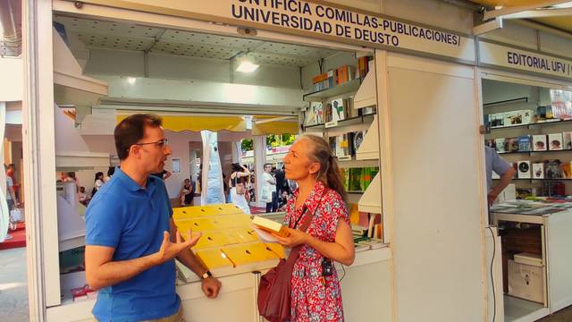 Two people engaging in a conversation at a book stall during a book fair.