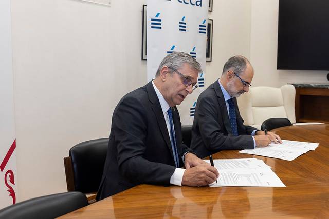 Dos hombres están firmando documentos en una mesa en una oficina.
