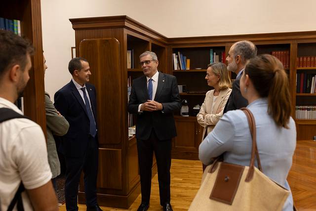 Un grupo de personas disfrutando de una conversación en un entorno formal con estanterías de libros de fondo.