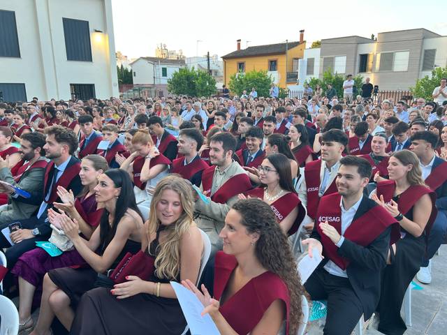 Un gran grupo de personas aplaudiendo en una ceremonia de graduación al aire libre.
