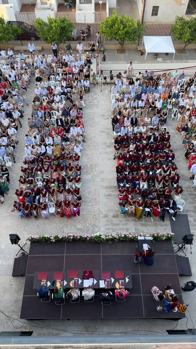 Una multitud de personas sentadas en un evento al aire libre, con un escenario en el frente.