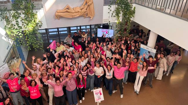 Un grupo grande de personas vestidas de rosa celebra en un espacio abierto con decoraciones y plantas.