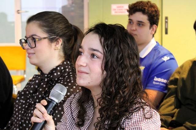 Un grupo de jóvenes en un evento, con una chica sosteniendo un micrófono y expresando interés.