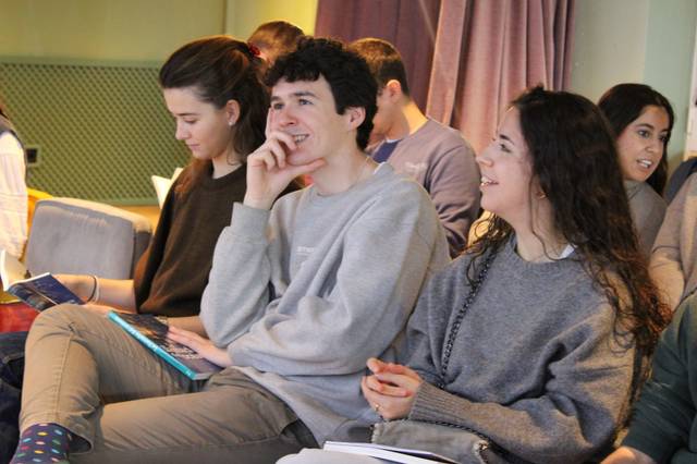 Un grupo de jóvenes sentados en un ambiente de aula, atentos y sonrientes durante una actividad.