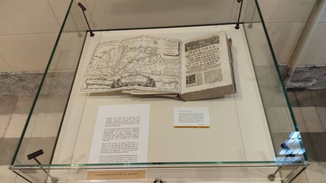 Un libro antiguo abierto se exhibe en una vitrina de vidrio.