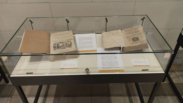 La imagen muestra una vitrina con libros antiguos y documentos en exhibición.