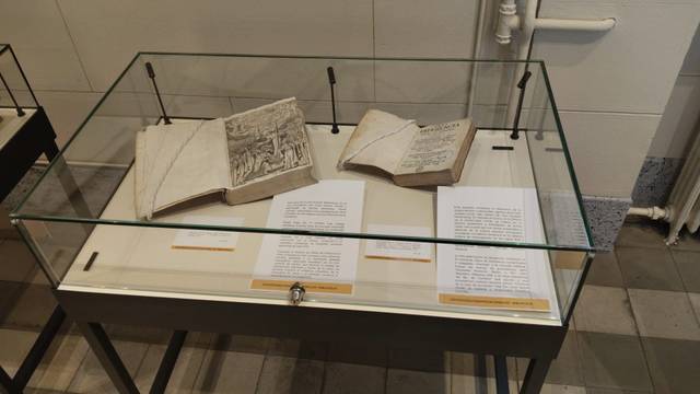 En la imagen se pueden ver varios libros antiguos exhibidos en una vitrina de vidrio.