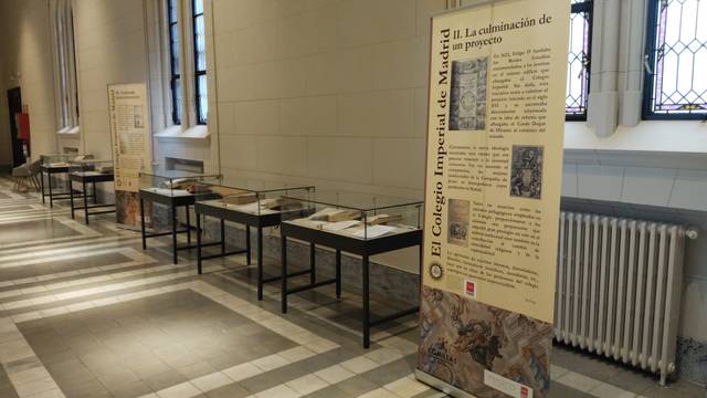 Una exposición en un pasillo con paneles informativos y vitrinas que exhiben objetos relacionados con la historia del Colegio Imperial de Madrid.