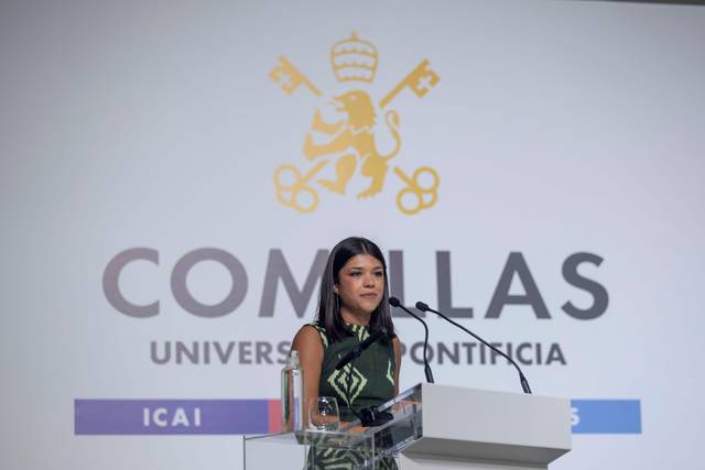 Una mujer presenta un discurso frente al logo de la Universidad Pontificia Comillas.