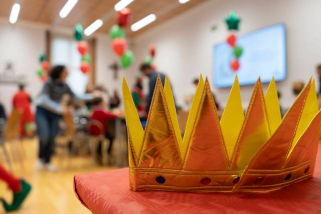 Una corona dorada en primer plano con un fondo desenfocado de personas en una fiesta con decoraciones de globos.