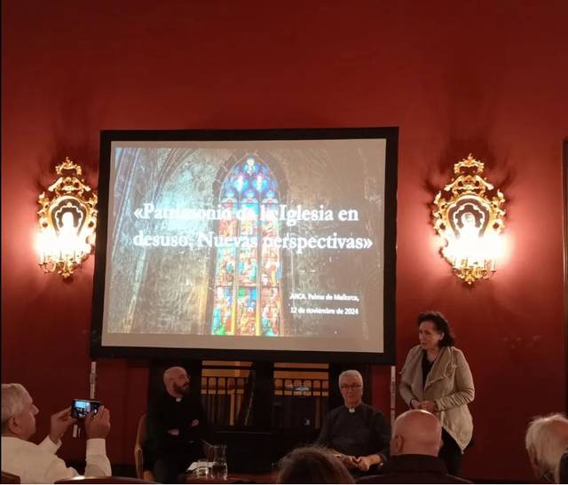 La imagen muestra a varias personas en lo que parece una conferencia o presentación en una sala elegante, con foco en una pantalla grande que muestra una presentación sobre patrimonio de la Iglesia.