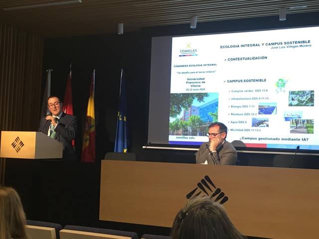 A man is giving a presentation on sustainable campus initiatives, while another man listens, in a conference room with a slide titled 'Ecología Integral y Campus Sostenible' displayed.