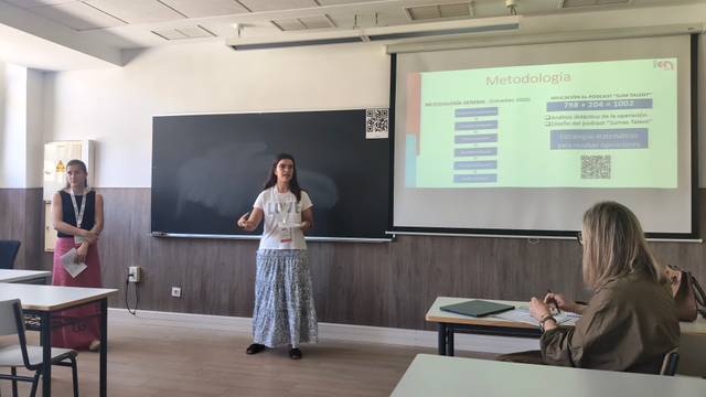 Una presentación académica en un aula donde dos personas exponen un tema ante un grupo pequeño.