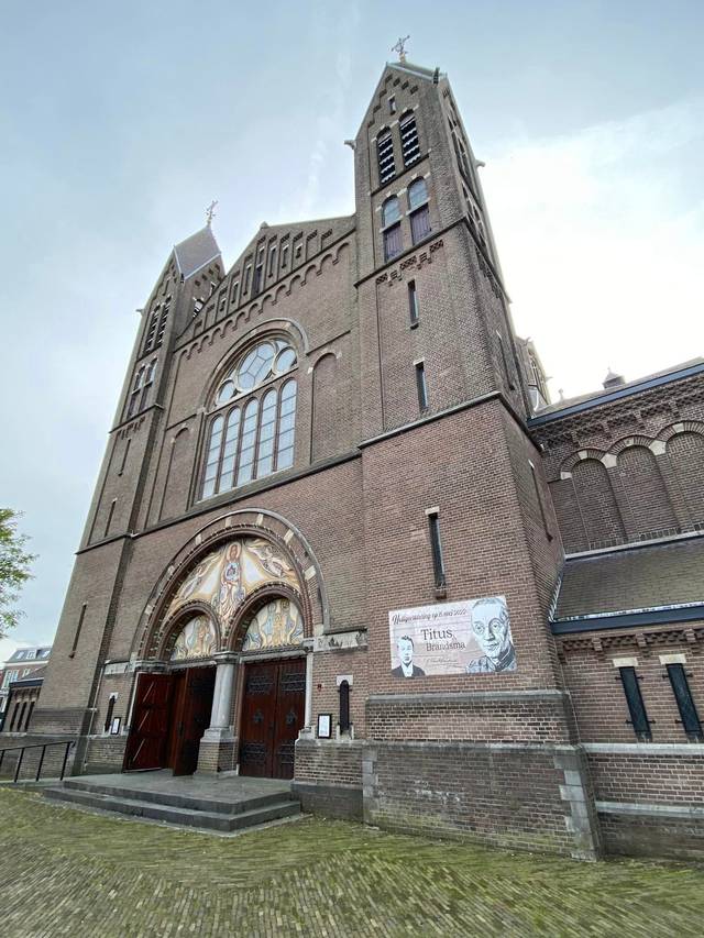 A view of a large brick church with a Gothic style entrance and a tall tower under a cloudy sky.