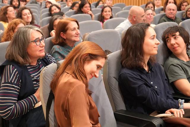 Un grupo de mujeres y hombres sentados en un auditorio, prestando atención a un evento o charla.