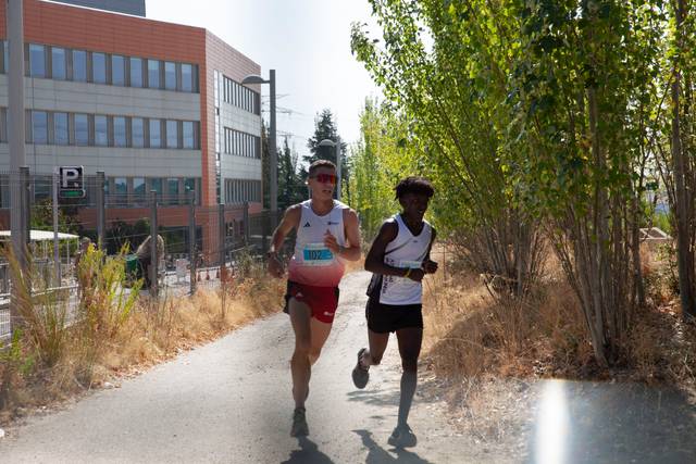 Dos corredores compiten en una ruta al aire libre en un día soleado.
