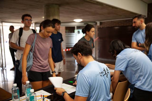 Un grupo de personas en un ambiente académico, algunas de pie y otras sentadas en una mesa, realizando actividades de registro.