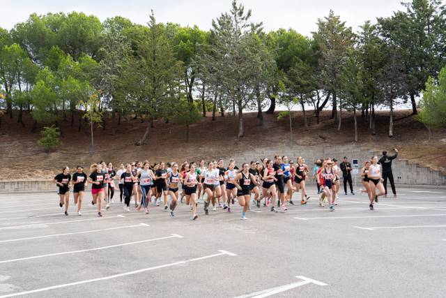 A group of women running in a race on a paved area with trees in the background.