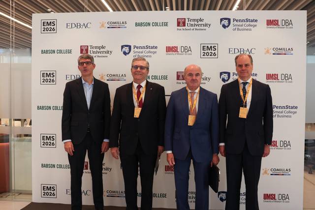 Cuatro personas posan frente a un fondo con logotipos de universidades y un evento académico.