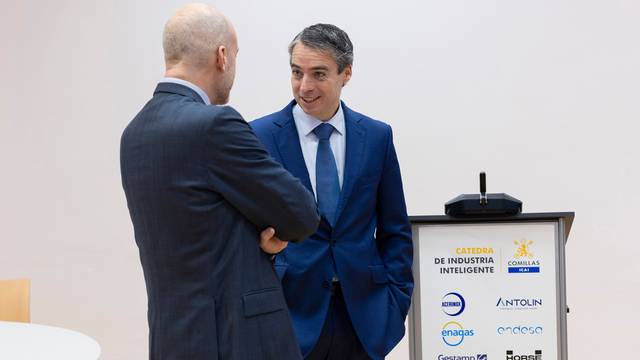 Dos hombres conversan durante un evento en un auditorio.