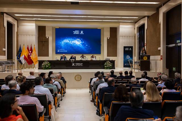 Una conferencia en una sala con un público atento y varios panelistas en el escenario.