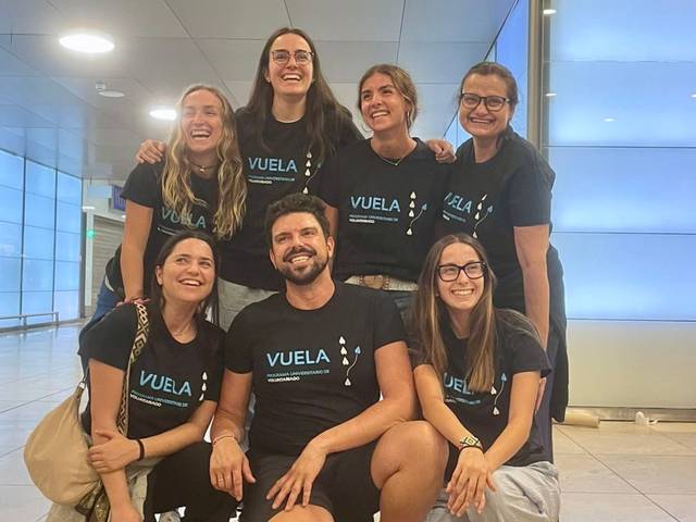 Grupo de amigos posando juntos en un lugar moderno, todos con camisetas negras que tienen la palabra 'VUELA'.