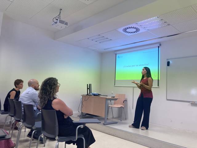 Una presentadora da una charla frente a un grupo de personas en una sala de conferencias.